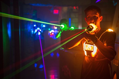 Drei Spieler in der neuen Lasertag Halle im Prater leuchten mit bunten Phasern und ihren Suits im Dunkeln in allen Farben.