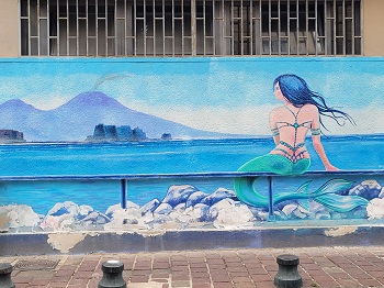 Auf eine Hauswand wurde eine am Ufer von Neapel sitzende Nixe mit Blick auf den Vesuv gemalt.