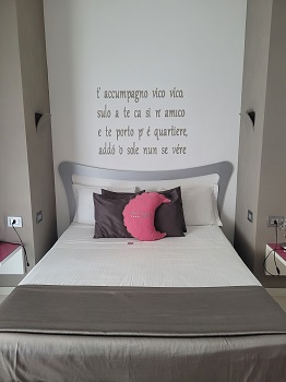 Hotelbett in grau und weiß mit pinkem Polster, an der Wand dahinter ein italienischer Liedtext