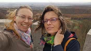 Zwei Frauen auf einer Aussichtswarte, hinter ihnen Wald und Stadt