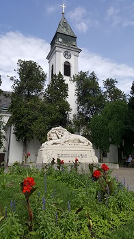 Löwendenkmal hinter roten Rosen vor einer Kirche