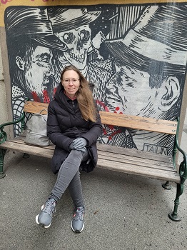 Frau sitzt auf Parkbank vor Wandmalerei mit zwei Männerköpfen und einem Skelett