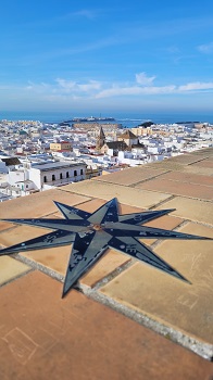 Eine Windrose auf einer Mauer weist die Himmelsrichtungen, dahinter die Dächer von Cádiz und das Meer