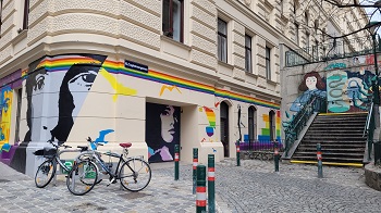 Mit Regenbogenfarben bemaltes Haus, dahinter eine Stiege mit Graffiti