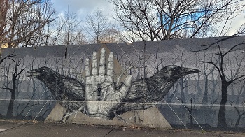 Zwei gezeichnete Raben und eine Menschenhand auf einer verfallenen Mauer