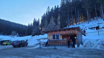 Holzhütte am Parkplatz, dahinter Schnee und Wald