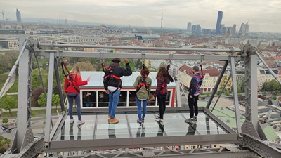 5 Menschen stehen auf der Glasplattform der Plattform 9 am Wiener Riesenrad und blicken auf ganz Wien hinunter