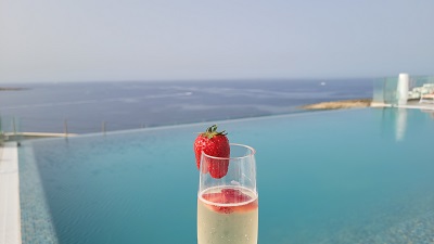 Sektglas mit Erdbeere vor Infinity Pool mit Meerblick auf Malta