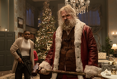 David Harbour als Santa schwingt den Hammer um sich der Geiselnehmer zu entledigen.