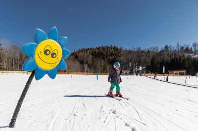 Mädchen fährt Ski im Anna-Land in Annaberg und an einer blauen Blume vorbei