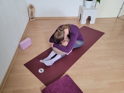 Frau beim Yin Yoga in sitzender Vorbeuge, auf Yogabolster gestützt