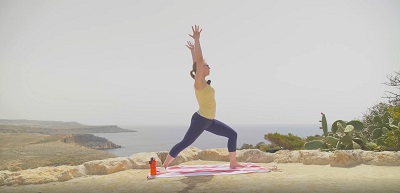 Yogalehrerin Sabrina Farkas zeigt mit Vinyasa Yoga einen der Yogastile auf einem Hügel im Krieger 1, im Hintergrund das Meer
