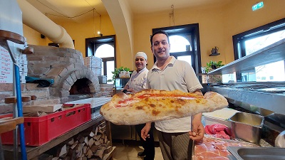 Pizzabäcker mit Pizza vor dem Holzofen im Il Sestante in der Piaristengasse