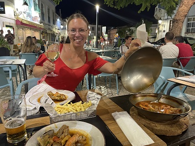 Frau mit Weinglas in der Hand im Gastgarten eines Restaurants mit der anderen Hand den Pfannendeckel