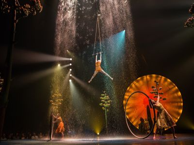 Trapezkünstlerin in künstlichem Wasserfall in der Luft, auf der Cirque du Soleil Luzia Bühne, unter ihr zwei Artistinnen in Cyr Wheels