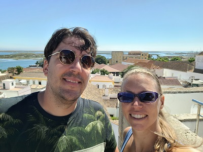 Frau und Mann mit Sonnenbrillen auf einem Kirchturm, im Hintergrund Gebäude und Meer