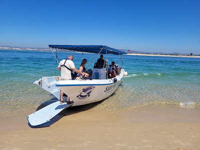 Ausflugsboot mit offener Heckklappe liegt im niedrigen, türkisblauen Wasser am feinen Sand