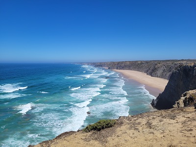 Ausblick auf von Felsen umgebene Sandbucht an der Algarve mit mittlerem Wellengang