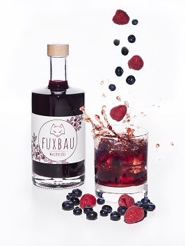 Eine Flasche Fuxbau Waldbeere Gin und ein Glas Gin in das Beeren fallen