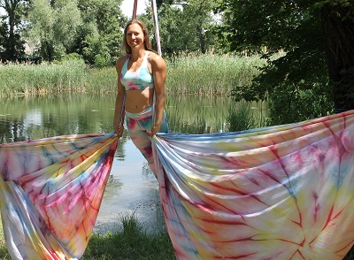 In Kamera lächelnde Frau in aufrechter Position mit buntem Silk vor Teich