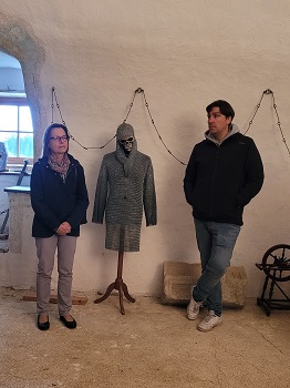 Frau und Mann stehen rechts und links neben einer Kleiderpuppe, die ein Kettenhemd und einen Totenkopf trägt