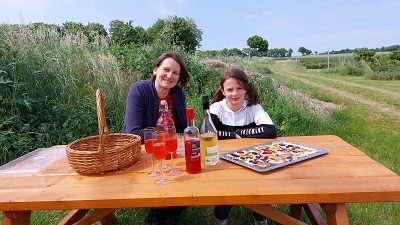 Katharina Hummel mit Tochter mit Brötchen und Himbeersturm an einem Tisch vor dem eigenen Biobeeren-Feld.