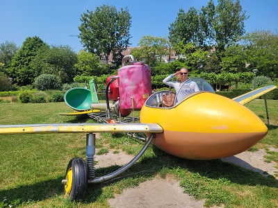 Frau salutiert in Skulptur eines gelben Flugzeug im Comicstil
