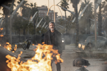 Ein Standbild aus dem Film Bird Box: Barcelona. Ein grauhaariger Mann geht auf Flammen im Vordergrund des Bildes zu.
