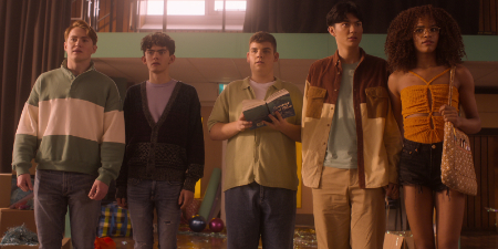 Eine Szene aus der zweiten Staffel Heartstopper. Von links nach rechts stehen Nick, Charlie, Isaac, Tao und Elle neben einander in einer Turnhalle. Die ganze Teenagergruppe sieht ein wenig verwirrt aus.