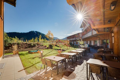 Die Sonne strahlt auf die Terasse im JUFA Hotel Annaberg, die Esstische und den Spielplatz