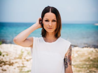 Christina Stürmer mit weißem T-Shirt und Strand im Hintergeund