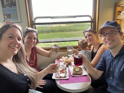 Drei Frauen, ein Mann und ein Baby genießen roten und weißen Spritzer, Brote und Mehlspeisen im Heurigenwaggon im Reblaus Express