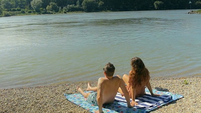 Pärchen sitzt mit Badeoutfit am Ufer der Orther Inseln an der Donau