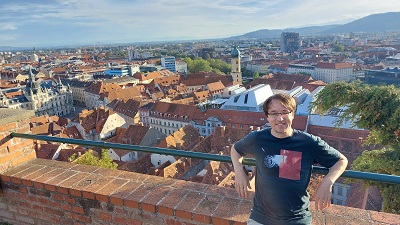 Mann steht bei Wand unterhalb des Uhrturms mit Panoramablick auf die Grazer Altstadt