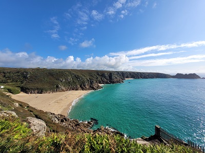 Blick auf goldfarbenen Strand und türkisblaues Meer, im Vordergrund niedrige Grünpflanzen und dahinter steile Klippen während der Cornwall Rundreise