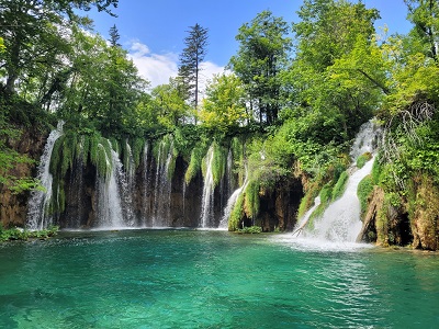Breiter, von Pflanzen umgebener Wasserfall, der in einem türkisen See mündet