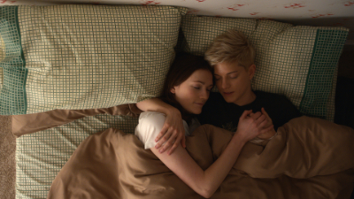 Letzter Eintrag auf unserer LGBTQ+ Serien und Filme Liste: George und Mae aus der Serie Feel Good liegen gemeinsam in einem Bett. Mae hat den Arm um George, die den Kopf auf Maes Brust hat.