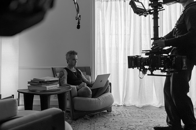 Robbie Williams sitzt mit Laptop auf einem Couchsessel und wird dabei gefilmt