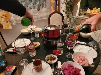 Hände zweier Männer beim Einschenken von Rotwein zum Fleisch Fondue