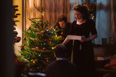 Eine Familie, bestehend aus Mutter, Vater und Sohn, schmückt fröhlich einen Weihnachtsbaum mit Ornamenten und Lametta.