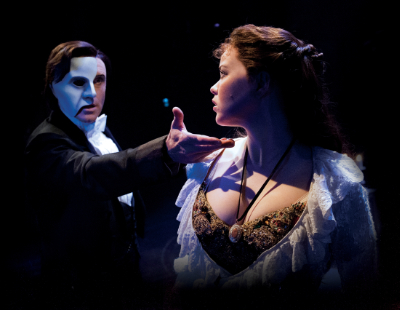 Ein Foto der Produktion von Das Phantom der Oper im Raimund Theater in Wien. Das Phantom trägt seine Maske und streckt seinen Arm nach Christine aus.