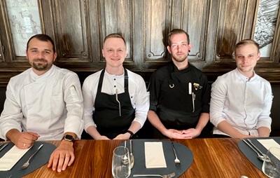Die Köche Deniz Neverov, Bram Rondhuis, Daniel Rössl und Dominik Czvitkovits sitzen im Handwerk Restaurant vor gedecktem Tisch