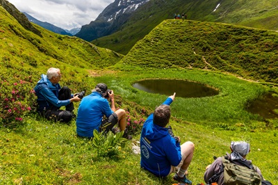 Karl Füsselberger von der Wiener Fotoschule mit drei Kursteilnehmern im Gebirge mit Blick hinunter auf einen kleinen Baggersee