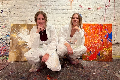 Verena und Kirstin, zwei Redakteurinnen der Helden der Freizeit, hocken vor ihnen bunten Action Paintings von Open the Door