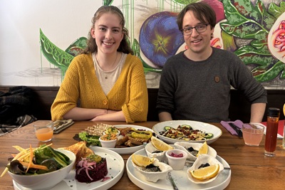 Frau und Mann vor einem voll gedeckten Tisch mit Beet Tatar, Faux Austern und Vorspeisentellern im Restaurant Tisch in Wien