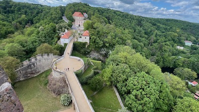 Blick auf zwei Brücken über mit Gras bedeckte Gräben. Eingebettet in eine Waldlandschaft.