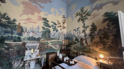 Ein Schlafzimmer. Ausgemalt mit einer Naturszenierie. Bäume, Felsenm, kleine Häuser, dramatischer bewölkter Himmel.