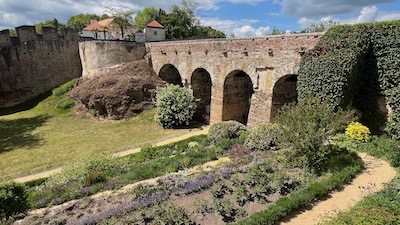 Eine Renaissancebrücke mit mehreren Rundbögen über einen mit Gras bewachsenen Graben. Davor kleine Terrassen eines Kräutergartens im Schloss Frain