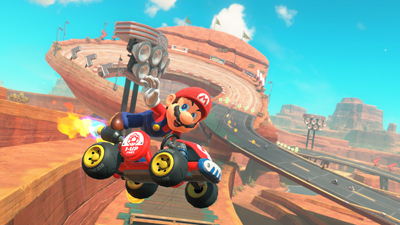 Mario springt in der Wüstenwelt von Mario Kart World in Richtung der Kamera und lächelt