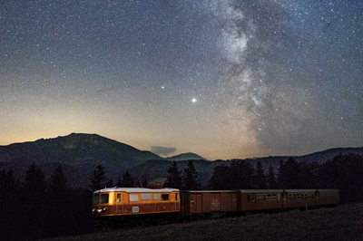 Ötscherbär Zug vor Bergpanorama und Sternenhimmel.